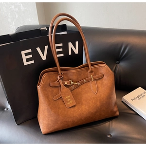 Detail of a brown leather tote bag featuring golden metal buckles and a textured finish
