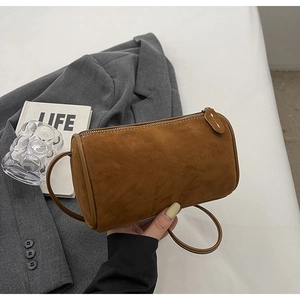 Detail of a brown suede cylinder bag with silver metal zipper and circular handles
