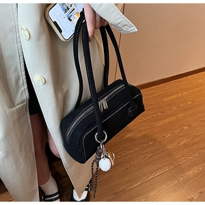 Detail of black canvas underarm bag featuring contrast white stitching and baseball charm