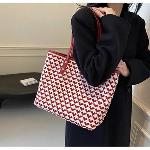 Detail of red heart-pattern tote bag with leather straps and gold rivets shown on shoulder