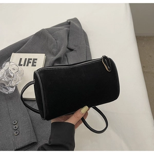Close-up of black suede barrel bag showing soft matte texture and minimalist zipper