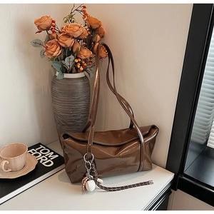 Close-up of brown glossy shoulder bag with a baseball charm and woven rope decoration