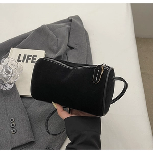 Detail of black suede cylindrical shoulder bag with silver zipper on a gray blazer background