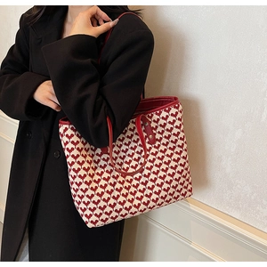 Detail of knit tote bag with heart patterns and red leather straps shown on a model