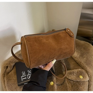 Detail of a brown suede cylinder crossbody bag showing the matte texture and fine stitching