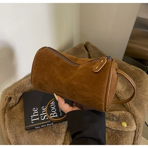 Detailed close-up of dark brown suede cylinder bag with premium leather handles and zipper
