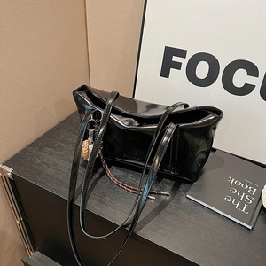 Glossy black patent leather tote bag with braided charm on vintage wooden table