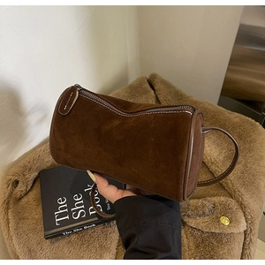 Detailed close-up of dark brown suede cylinder bag with white contrast stitching accents