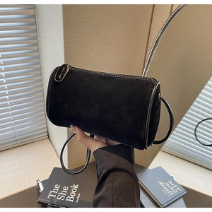Close-up of minimalist black suede cylinder bag with round strap and metal zipper detail