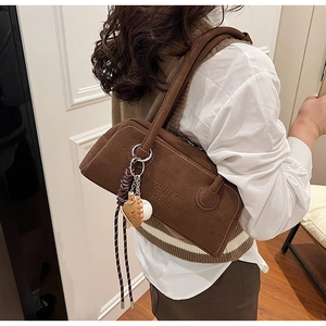 Detail view of brown suede shoulder bag with unique baseball charm and embossed texture