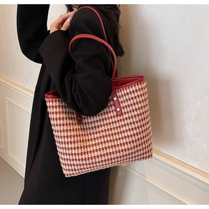 Close-up of red and white houndstooth tote bag with leather straps on model's shoulder