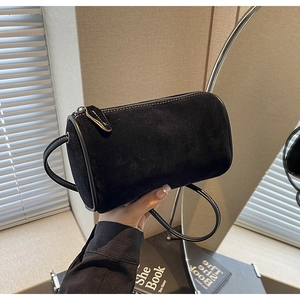 Detail showing the matte suede texture and leather piping of the black cylinder bag