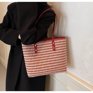 Detail of red houndstooth tote bag with leather handles and gold rivet accents