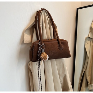 Detail of a dark brown suede cylindrical underarm bag with unique baseball glove charm