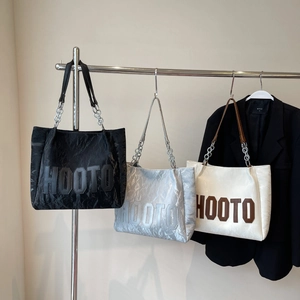 Détail de grands sacs fourre-tout en noir, argent et beige avec texture métallique et chaîne