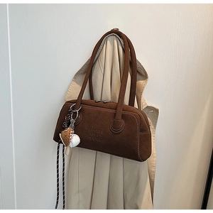 Detail view of dark brown suede shoulder bag with embossed logo and baseball charm