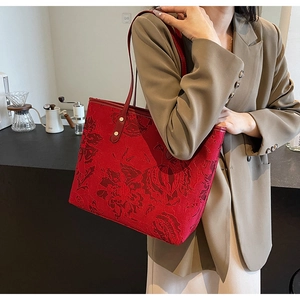 Red tote bag with embossed floral texture and gold rivets worn by a model in lifestyle setting
