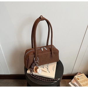 Detailed macro of dark brown suede shoulder bag with baseball charm on a wooden stool