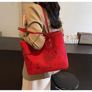 Detail of red tote bag with floral embossing shown on model in a modern cafe setting