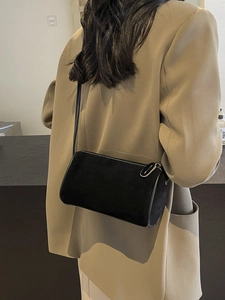 Minimalist black cylinder crossbody bag with white contrast stitching on model's shoulder