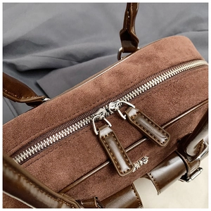 Close-up of brown suede Boston bag showing dual metal zippers and premium leather details