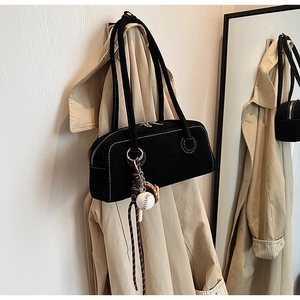 Detail of black shoulder bag with contrast stitching and baseball charm on trench coat