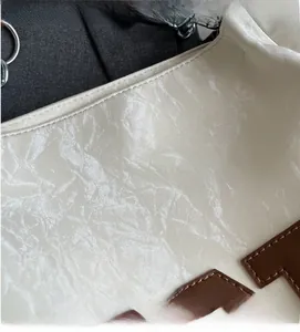 Détail du tissu blanc cassé texturé et de l'écusson en cuir marron du sac cabas