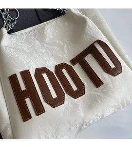 Détail du sac cabas blanc brillant avec lettres HOOTU en cuir marron et chaîne en métal