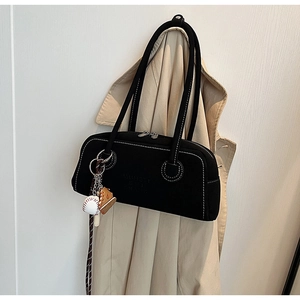 Close-up of black suede shoulder bag featuring white contrast stitching and baseball charm