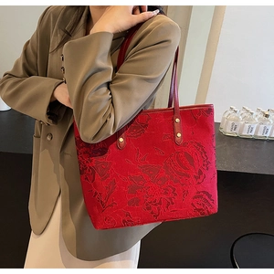 Detail of red jacquard tote bag with floral texture, gold rivets, and slim shoulder straps