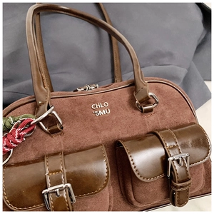 Detailed close-up of retro brown suede bowling bag with twin buckle pockets and metal logo
