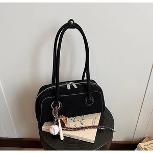 Close-up of black canvas underarm bag with white stitching and baseball charm on a chair