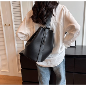 Rear view of a black pebbled leather bucket bag with a wide strap in a modern home setting