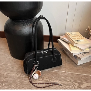 Detail of black underarm bag with white stitching, baseball pendant and embossed logo
