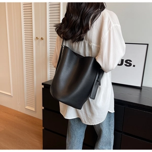 Model wearing a large black leather bucket bag with litchi grain texture and a strap