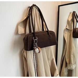 Macro detail of brown suede shoulder bag with white stitching and baseball charm