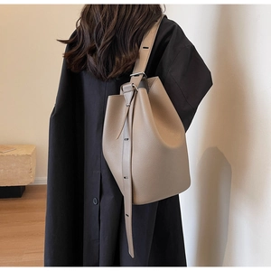 Taupe pebbled leather bucket bag styled on shoulder over a black oversized coat