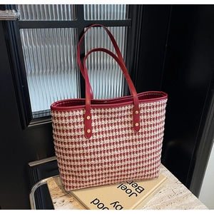 Detailed shot of red houndstooth tote bag with leather handles on a stone surface