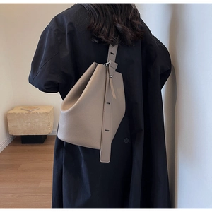 Back view of a khaki bucket bag in litchi grain leather on model's shoulder in minimalist room