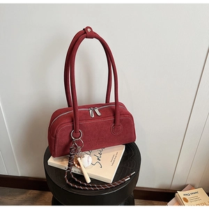 Detail of burgundy suede shoulder bag with dual metal zippers and a baseball charm