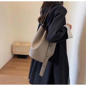 Detail of taupe large capacity bucket bag with lychee grain leather texture on model