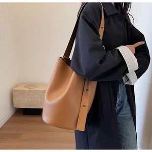 Model wearing a caramel brown pebble leather bucket bag with an adjustable wide strap