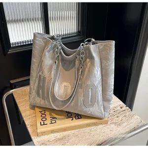 Gros plan d'un sac cabas argenté texturé avec écusson HOTO et bandoulière en chaîne métal