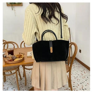 Detail of black suede tote bag with gold metal clasp and leather strap in cafe setting