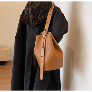 Brown pebble leather bucket bag side view on model wearing a black winter coat