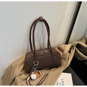 Close-up of dark brown suede shoulder bag with dual silver zippers and baseball charm