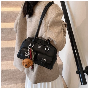 Detail of black leather shoulder bag featuring silver buckle pockets and plush dog charm