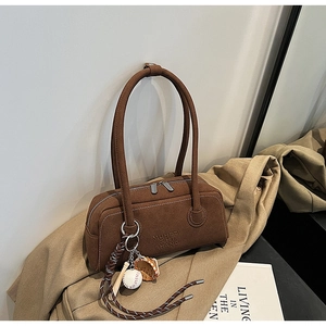 Detail of a brown suede underarm bag with unique baseball charm on a khaki trench coat