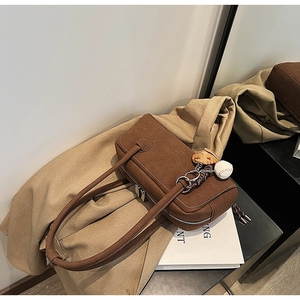 Close-up of brown suede shoulder bag with dual handles and baseball glove charm