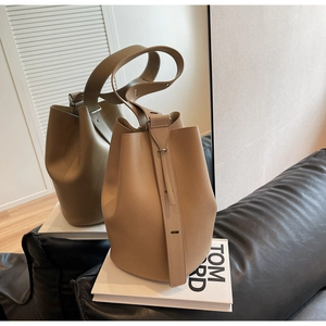 Detail of khaki lychee grain leather bucket bag with wide strap on a leather sofa